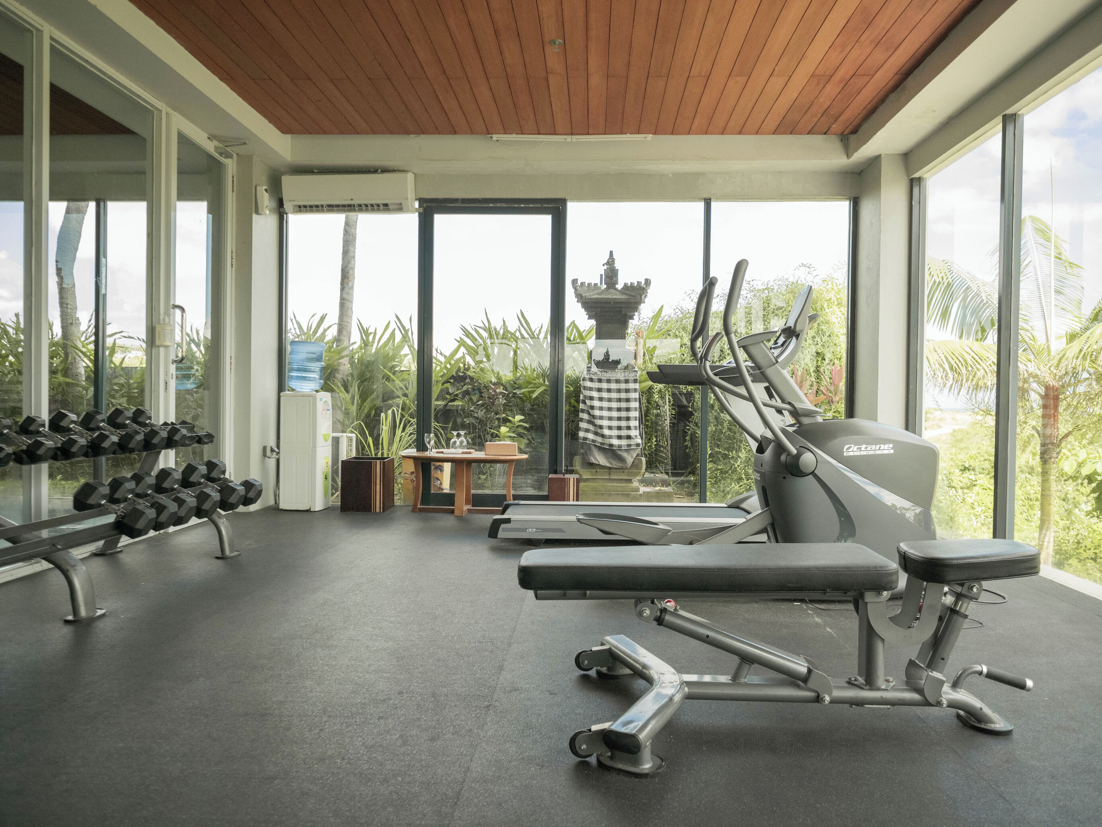 Un gimnasio con equipamiento de ejercicio, un dispensador de agua y una estatua al fondo.