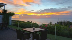 Eine Terrasse mit Tisch und Stühlen, mit Blick auf einen Sonnenuntergang über dem Meer.