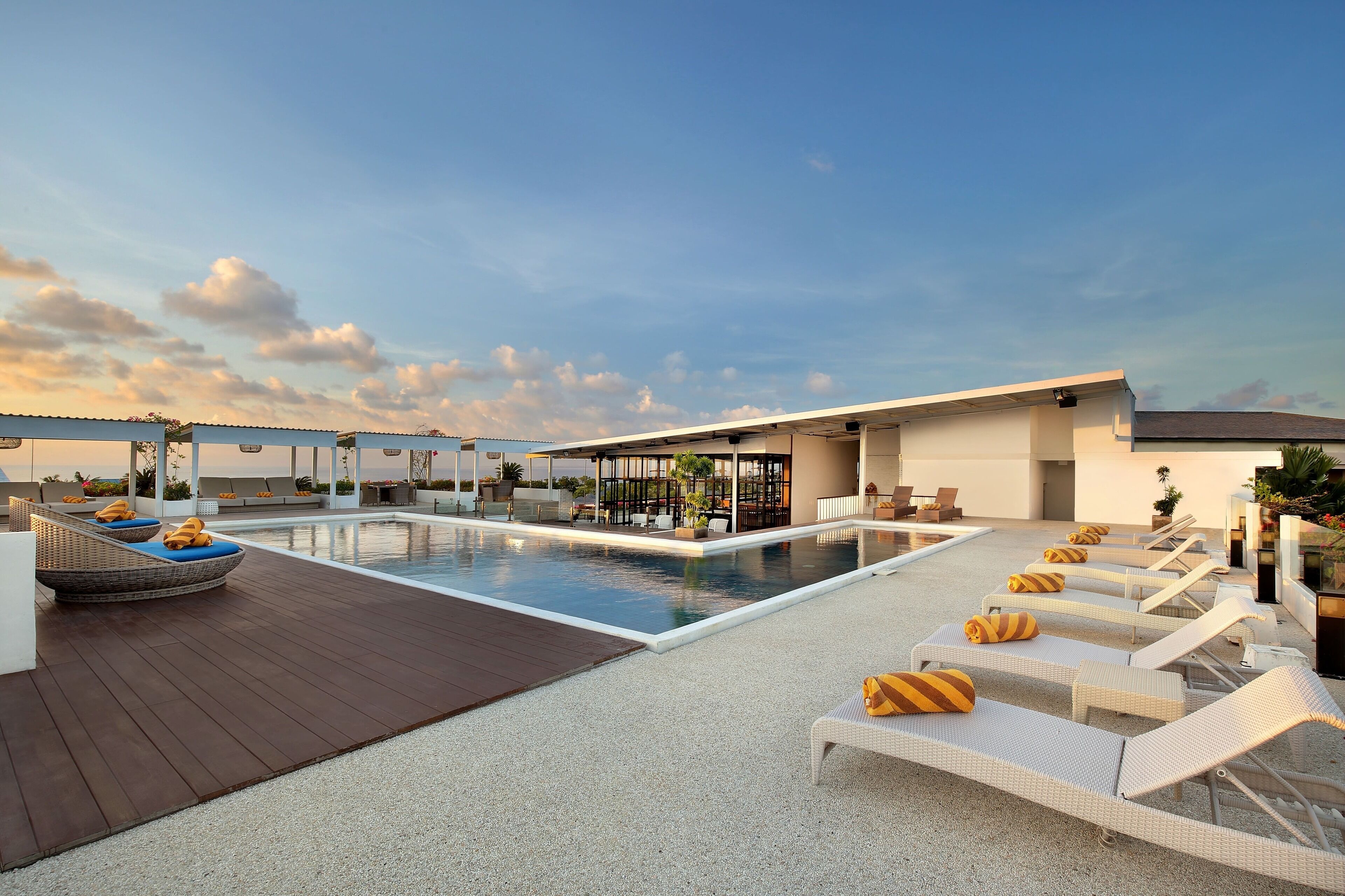 Un área de piscina en la azotea con sillones de descanso y una terraza de madera.