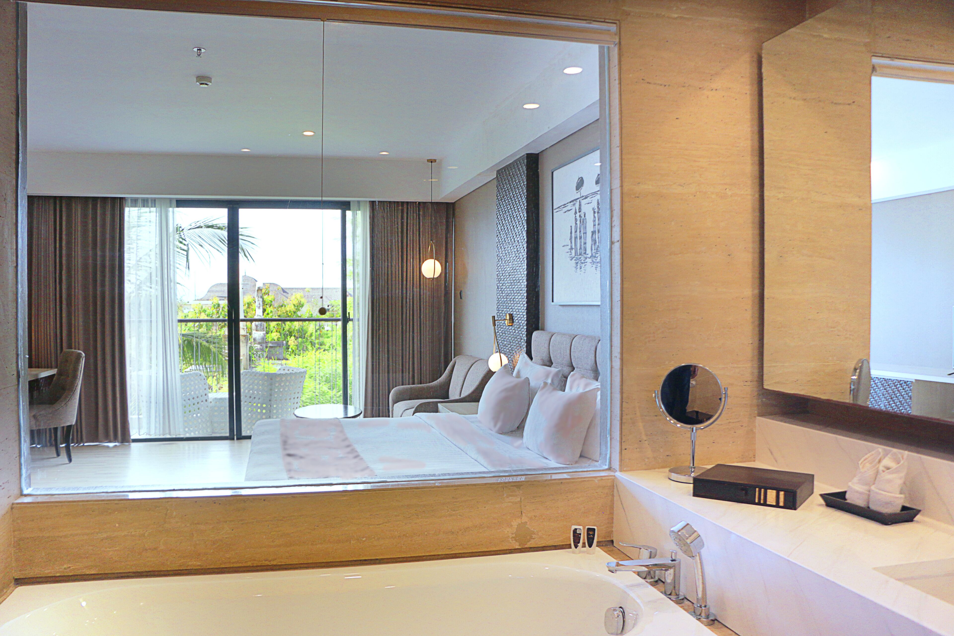 A modern hotel room with a large bed, a bathroom with a bathtub, and a balcony with outdoor furniture.