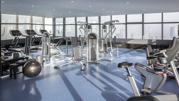 Ett modernt gym med olika typer av träningsutrustning, stora fönster och utsikt över staden.