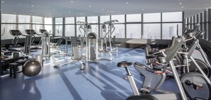 Une salle de sport moderne dotée de divers équipements d’exercice, de grandes fenêtres et offrant une vue sur la ville.