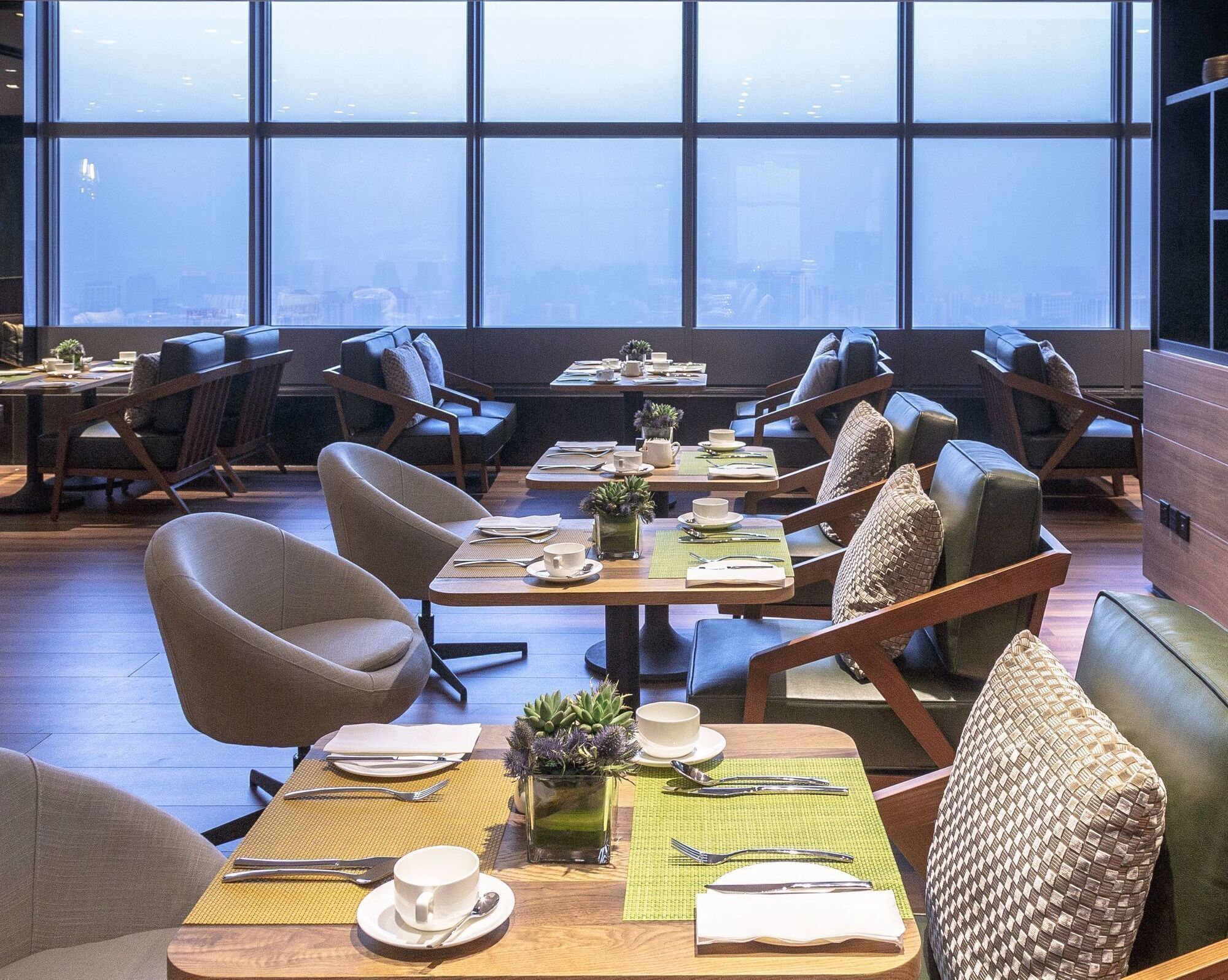 A modern dining area with multiple tables and chairs, large windows with a city view, and a clean, minimalist design.