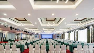 Un salón de conferencias con filas de mesas y sillas, un escenario con una pantalla y una alfombra roja.