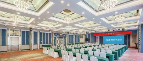 A conference room with rows of tables and chairs, a stage, and a large screen.