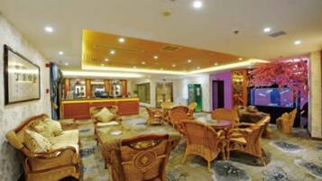 A hotel lobby with wicker furniture, a reception desk, and a television.