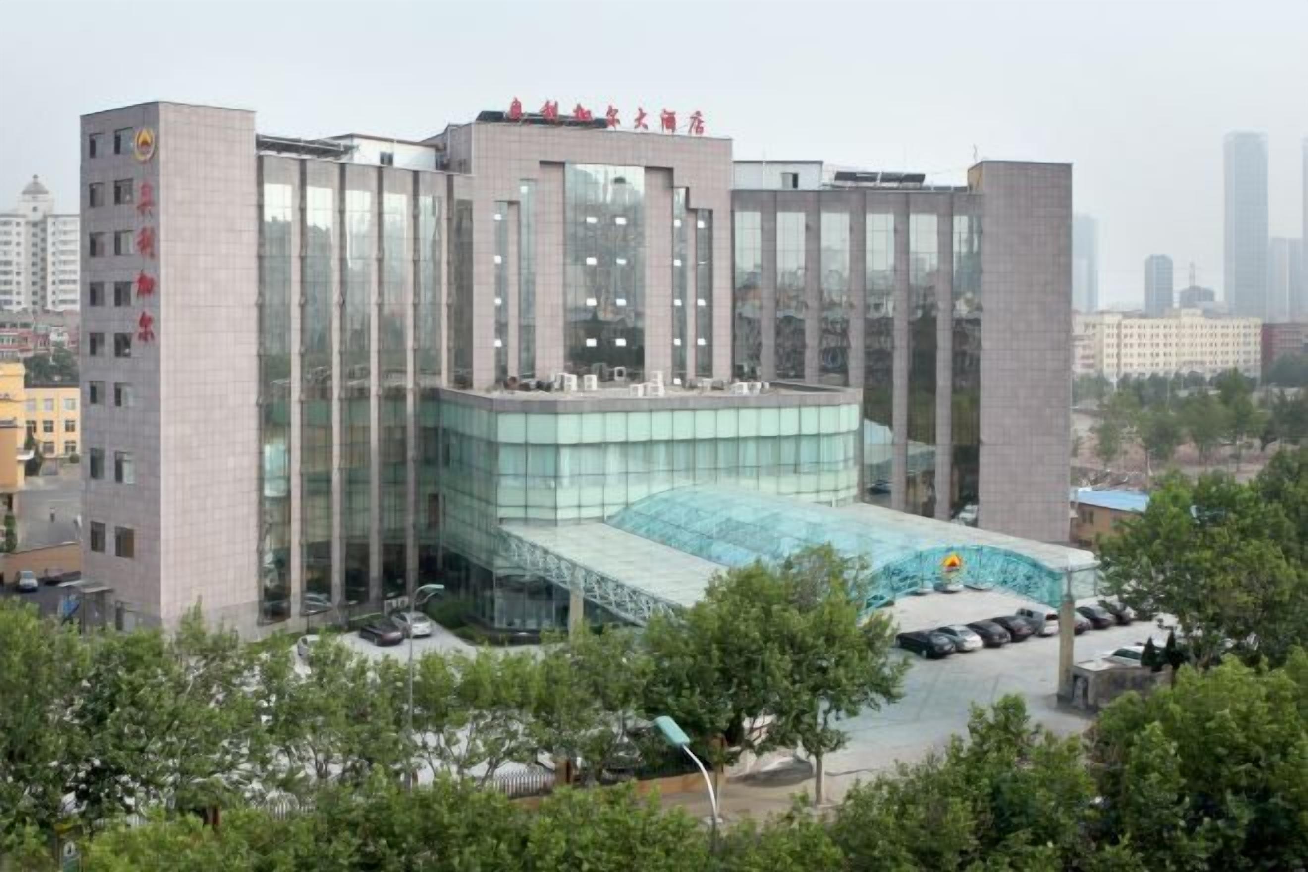 A modern building with a glass facade, a rooftop pool, and a parking area.