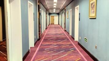 Ein Hotelgang mit einem gemusterten Teppich, Türen an beiden Seiten und gerahmten Bildern an den Wänden.