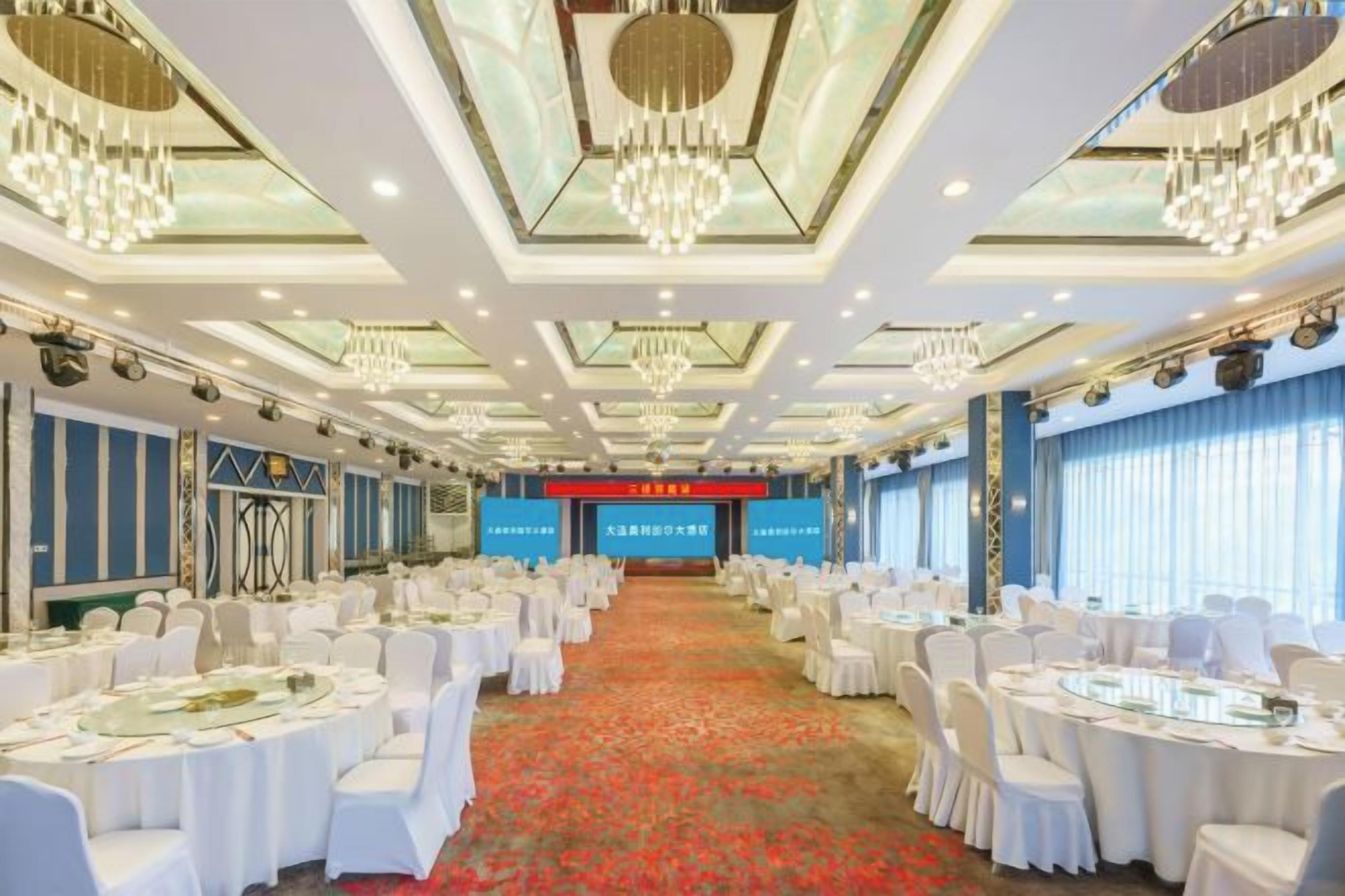 Un salón de banquetes con mesas redondas, sillas blancas y candelabros.