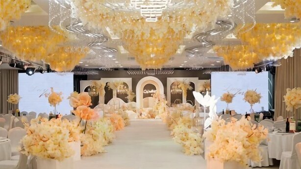 Un espacio con escenario, arreglos florales y zona de estar.
