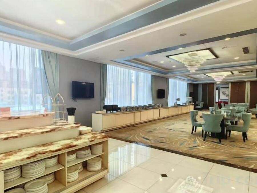 A spacious hotel lobby with a long reception desk, seating area, and a large window providing natural light.