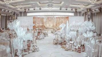 A formal event space with a stage, floral decorations, and a white carpet.
