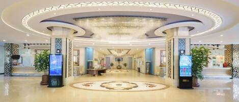 A spacious lobby with a central reception desk, a chandelier, and a circular decorative floor pattern.