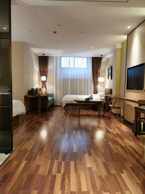 A hotel room with a wooden floor, a bed, a desk, a chair, a TV, and a window with curtains. - Andersen Culture (Shanghai)