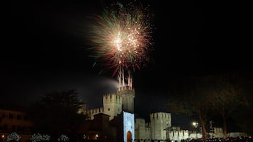 A historic castle with a tall tower, illuminated by lights, and a crowd gathered in front.