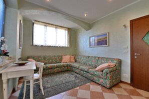 Une pièce comprenant une table à manger, un canapé à motifs floraux, un tapis à dessins, un tableau accroché au mur et une porte en bois.