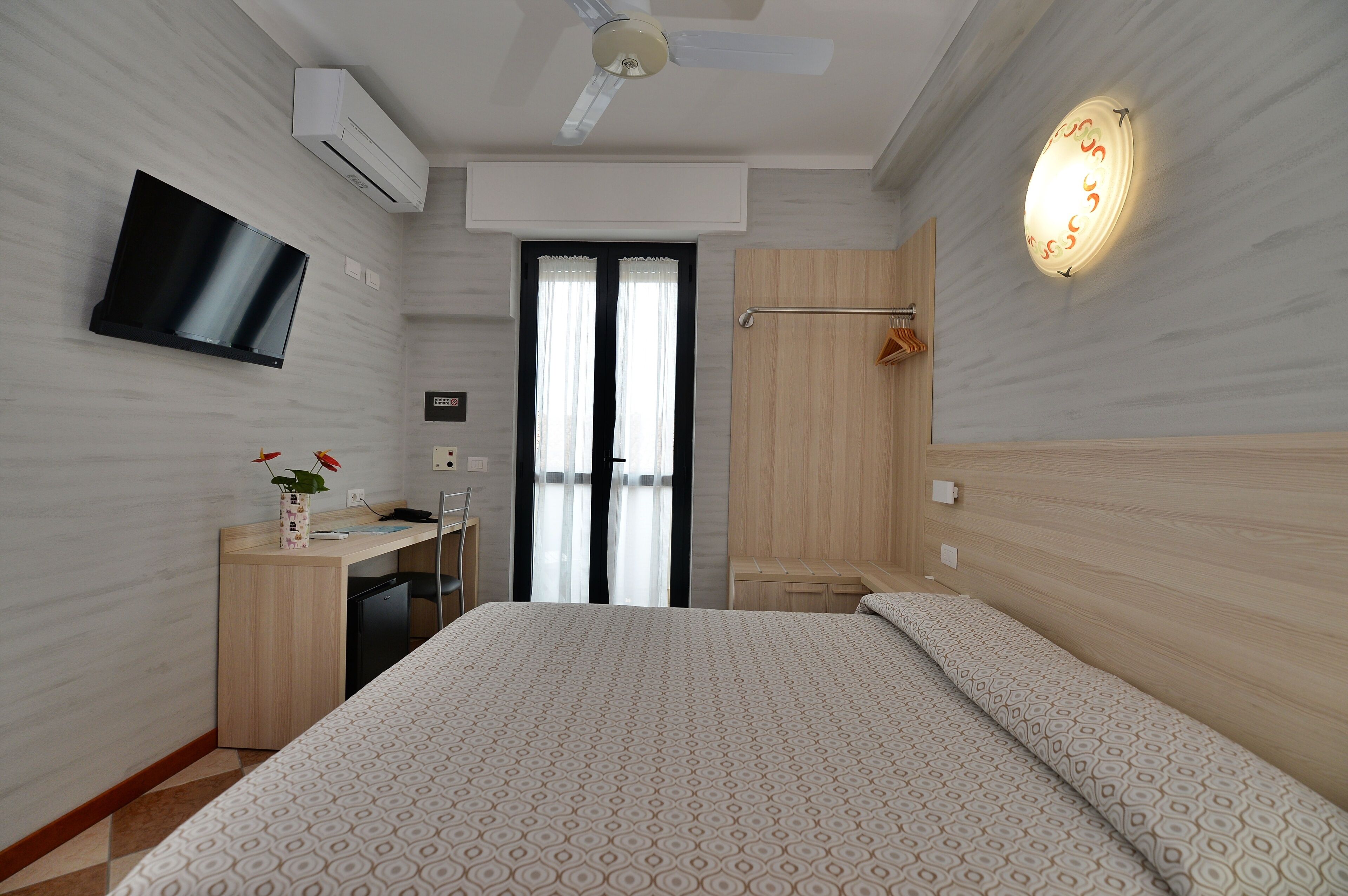 Una habitación de hotel moderna con cama, escritorio, televisión y ventilador de techo.