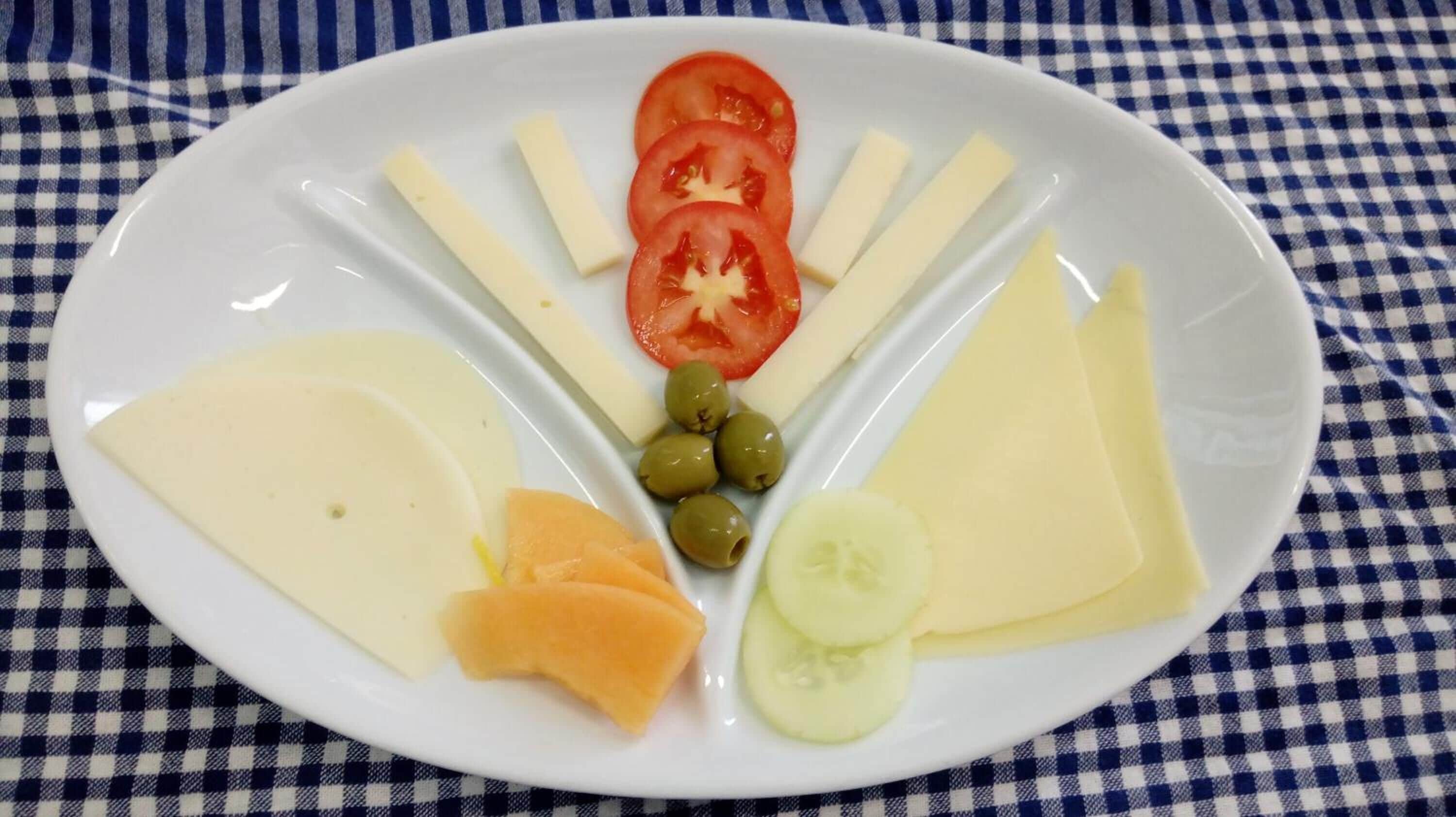 Un plato con queso, tomates, aceitunas, pepino y rodajas de melón.