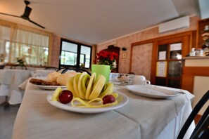 Une table de petit-déjeuner avec une assiette de fruits, une tasse verte et une assiette blanche.