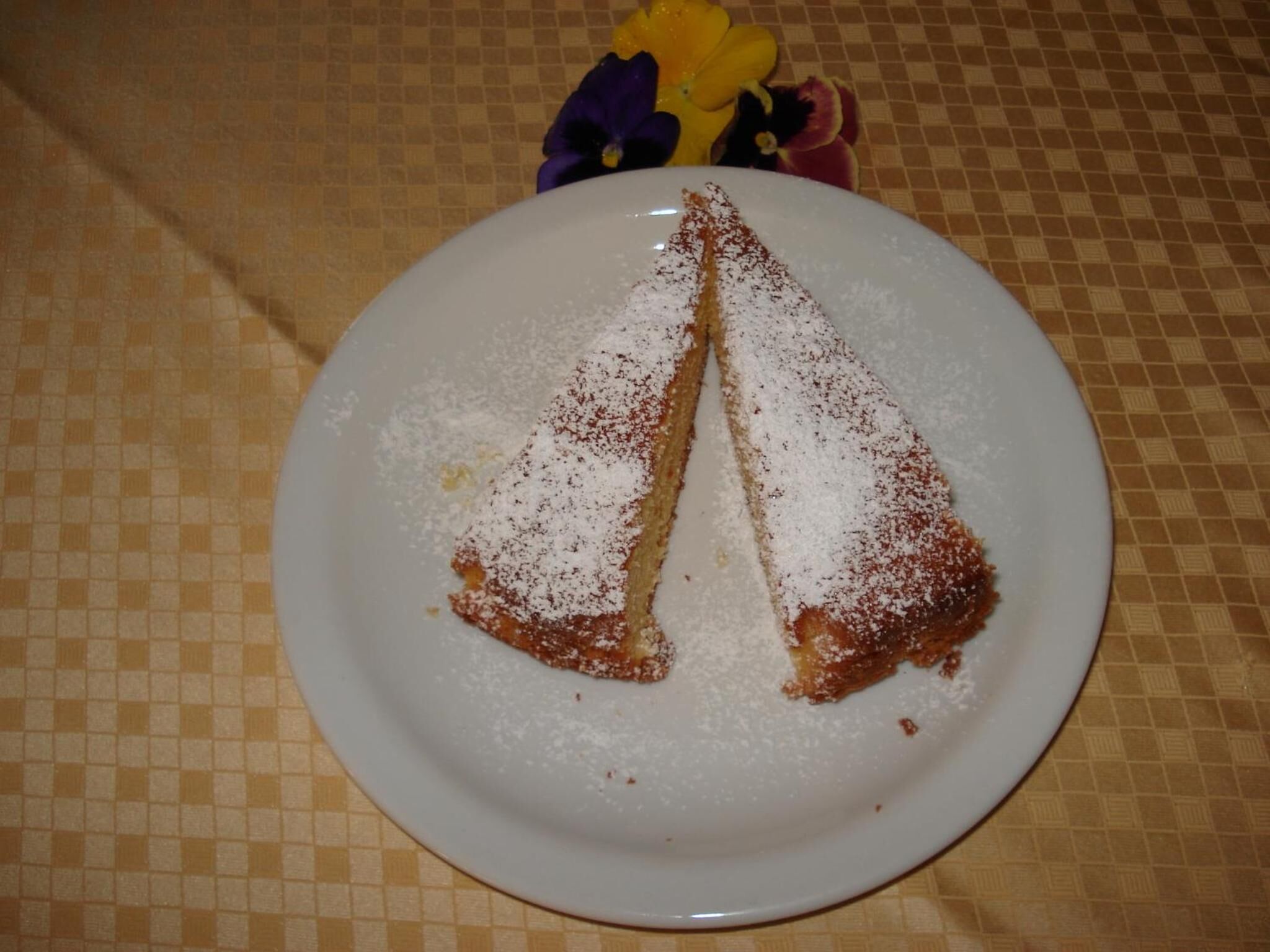 Un plato con un pastel triangular espolvoreado con azúcar glas, sobre una mesa con mantel a cuadros.