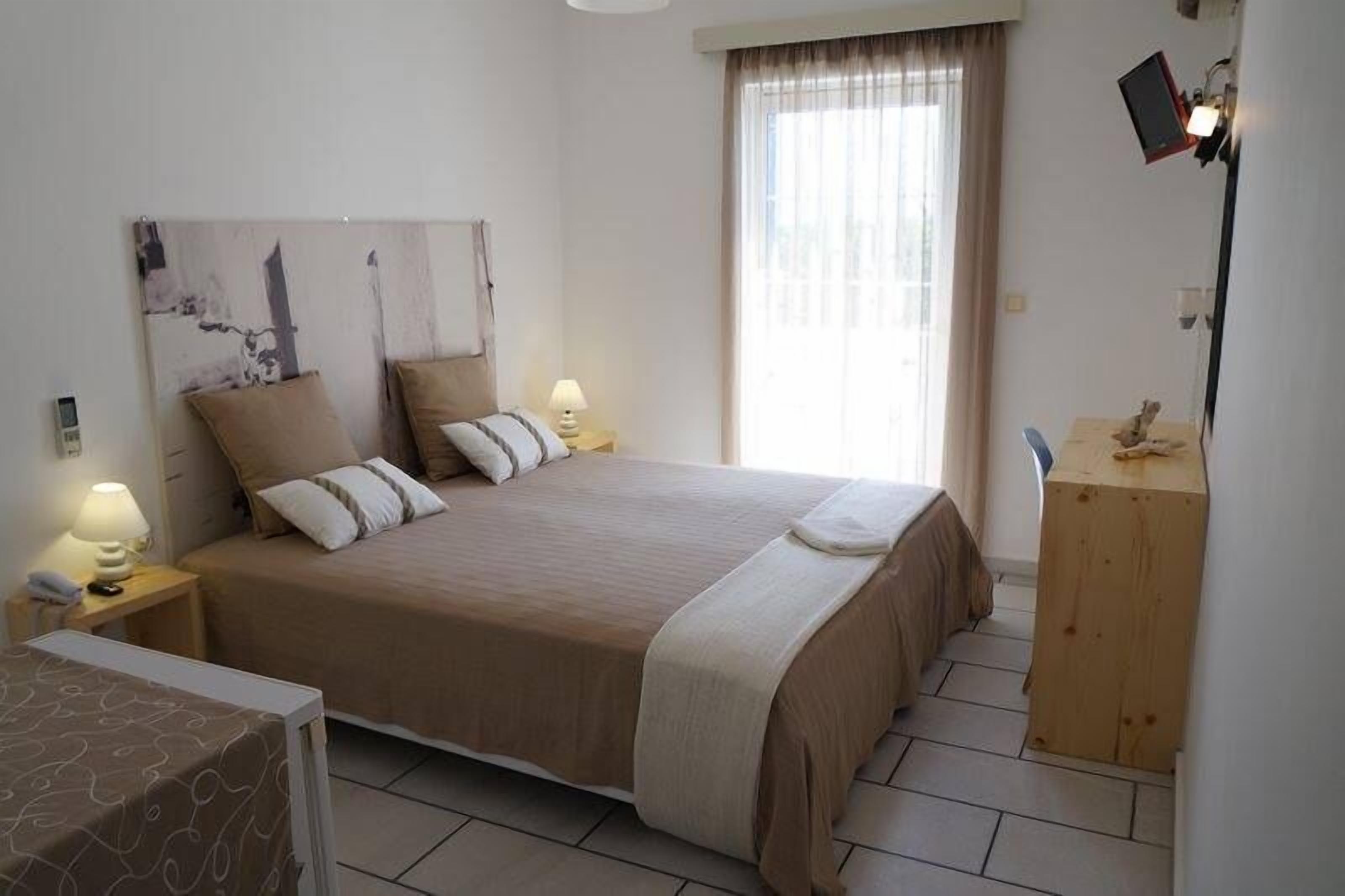 Un dormitorio ordenado con una cama grande, lámparas de noche, una mesita de madera y una ventana con cortinas.