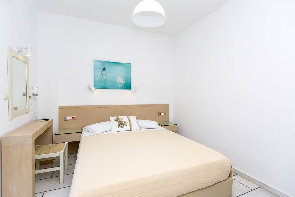 A neatly arranged bedroom with a bed, bedside tables, a desk, and a chair.