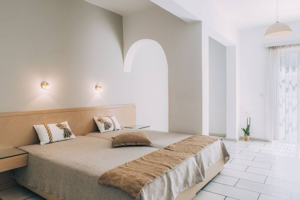 A modern bedroom with a large bed, two wall-mounted lights, a wooden headboard, and a potted plant.