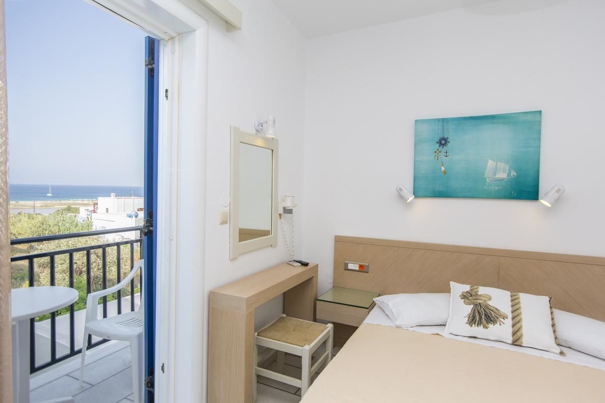 Habitación de hotel con balcón, cama con dos almohadas, mesita de noche, espejo y un cuadro.