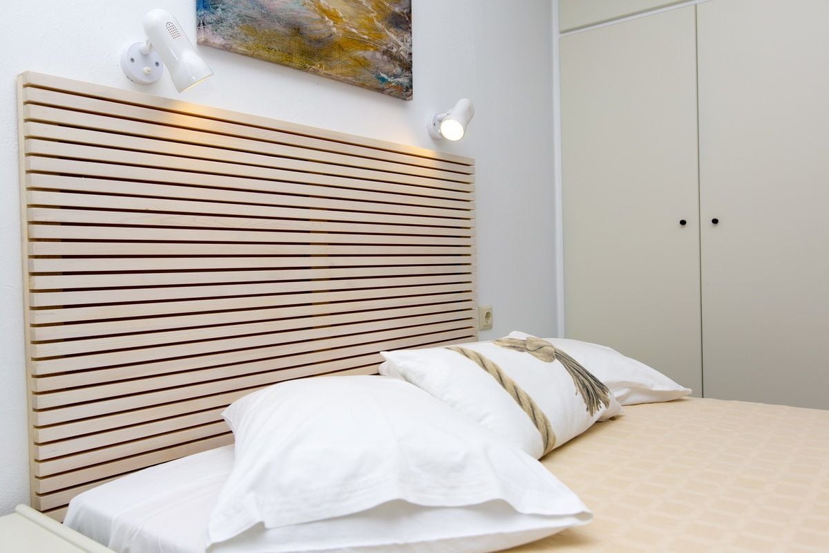 A bedroom with a wooden slatted headboard, white bedding, and a painting on the wall.