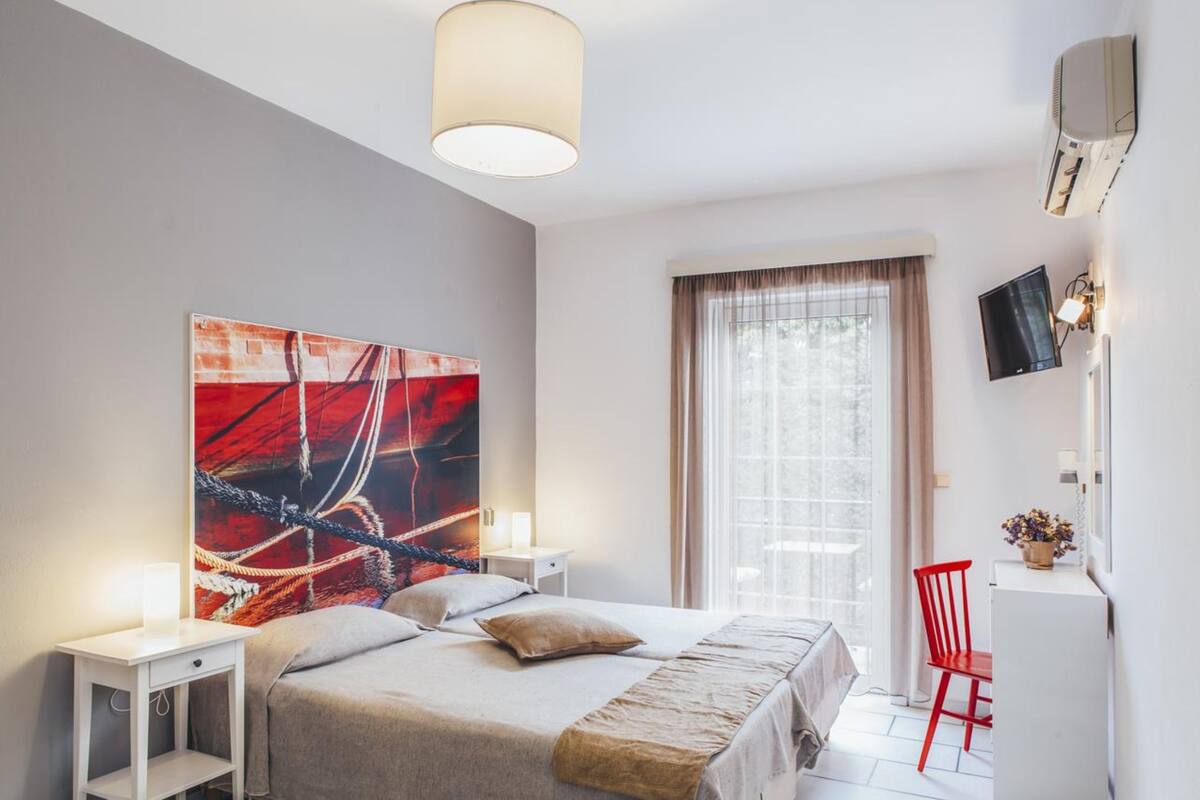 A modern hotel room with a large bed, bedside tables, a desk, a chair, and a TV.