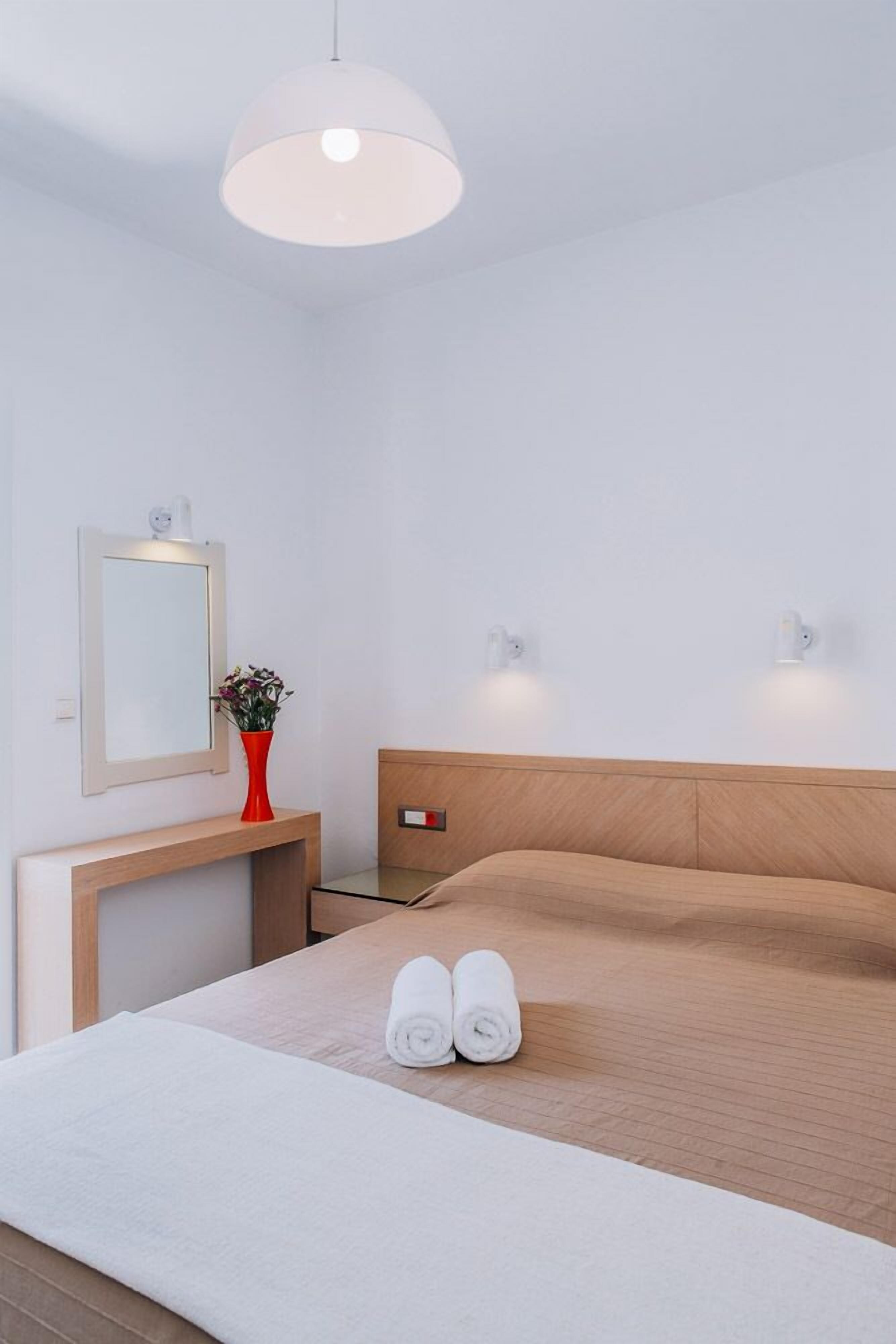 Una habitación de hotel moderna con una cama, una mesita de noche con un florero, un espejo e iluminación en la pared.