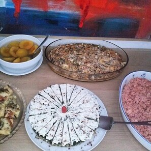 A table with various dishes including a pie, a bowl of fruit, and a dish with minced meat. - Semeli Hotel (Naxos)