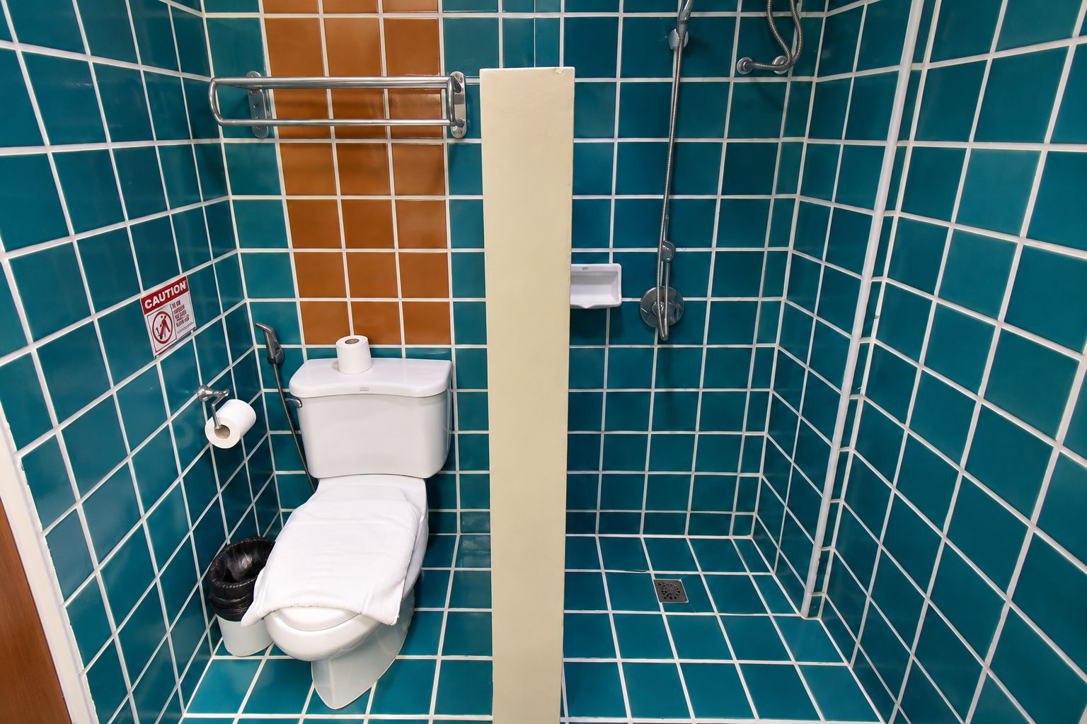 Un baño con inodoro, ducha y un letrero de precaución en la pared.