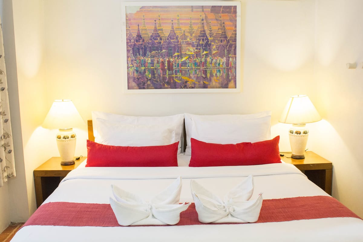 Een hotelkamer met een bed, twee nachtkastjes met lampen, een schilderij aan de muur en een rode en witte spreideken.