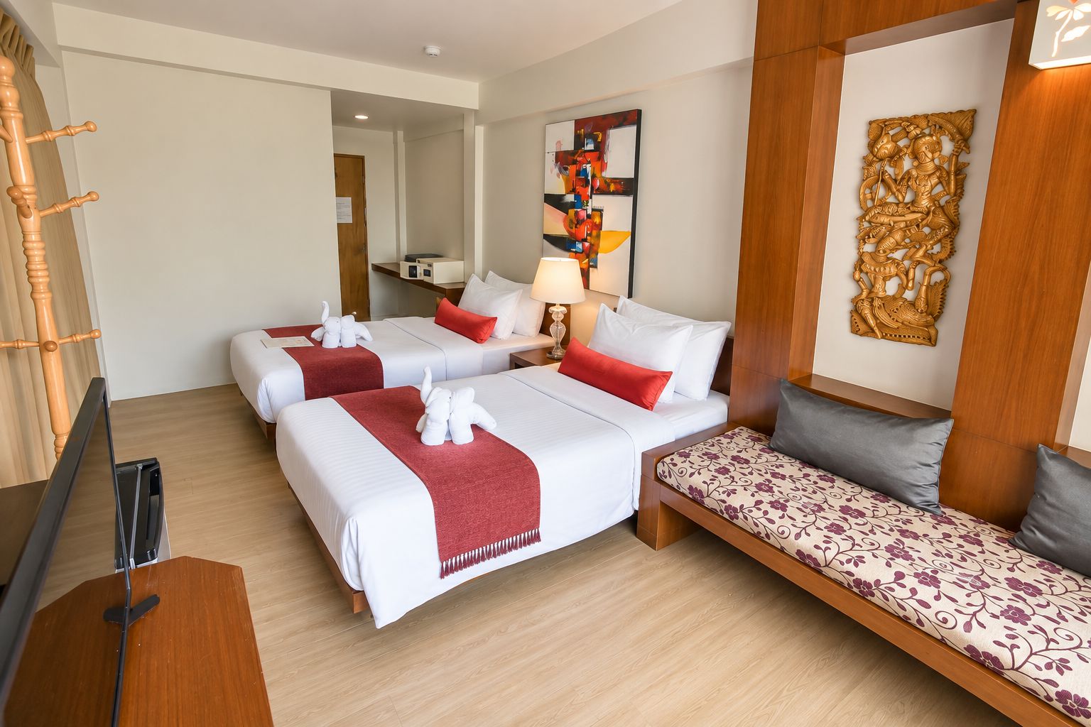 Habitación de hotel con dos camas, un sofá, piso de madera, pared con panel decorativo y un espejo.