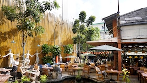 Un espace extérieur aménagé pour les repas, avec des tables et des chaises, un petit étang avec des carpes koï et des statues décoratives.