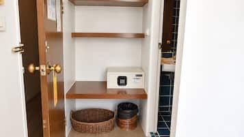 Un pasillo estrecho con una puerta a la izquierda, una pared blanca con un tablón de anuncios y una pared con azulejos azules a la derecha. Hay dos estantes de madera, uno de los cuales tiene un microondas.