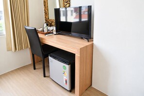 A compact hotel room with a wooden desk, a black chair, a small refrigerator, and a television. - Villa Cha Cha Banglumphu (Bangkok)