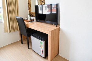 Habitación de hotel compacta con un escritorio de madera, una silla negra, un refrigerador pequeño y un televisor.