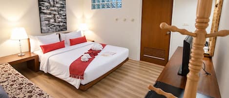 A hotel room with a bed, bedside tables, a TV, a wooden wardrobe, a window with blinds, and a painting on the wall.