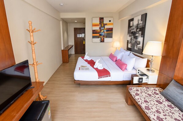 Una habitación de hotel con una cama, mesitas de noche, televisión, perchero de madera y obras de arte en las paredes.