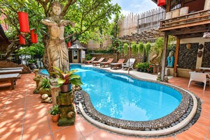 Una piscina con borde de piedra, rodeada de sillas de descanso y plantas en macetas.