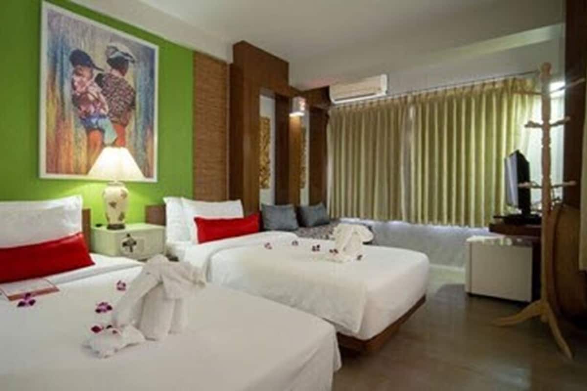 Een hotelkamer met twee bedden, een groene accentmuur, een schilderij, een lamp en een televisie.