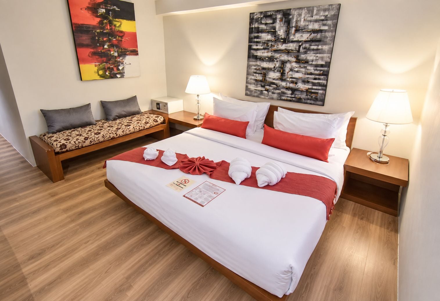 A hotel room with a large bed, a sofa, two bedside tables with lamps, and artwork on the walls.