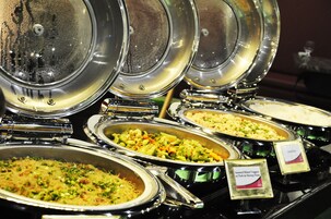 Een buffet met diverse gerechten, waaronder een bord met roerbakgroenten, varkensvlees en garnalenpasta.