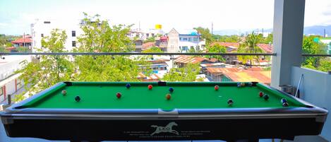A pool table with balls, a balcony, and a view of buildings and trees.