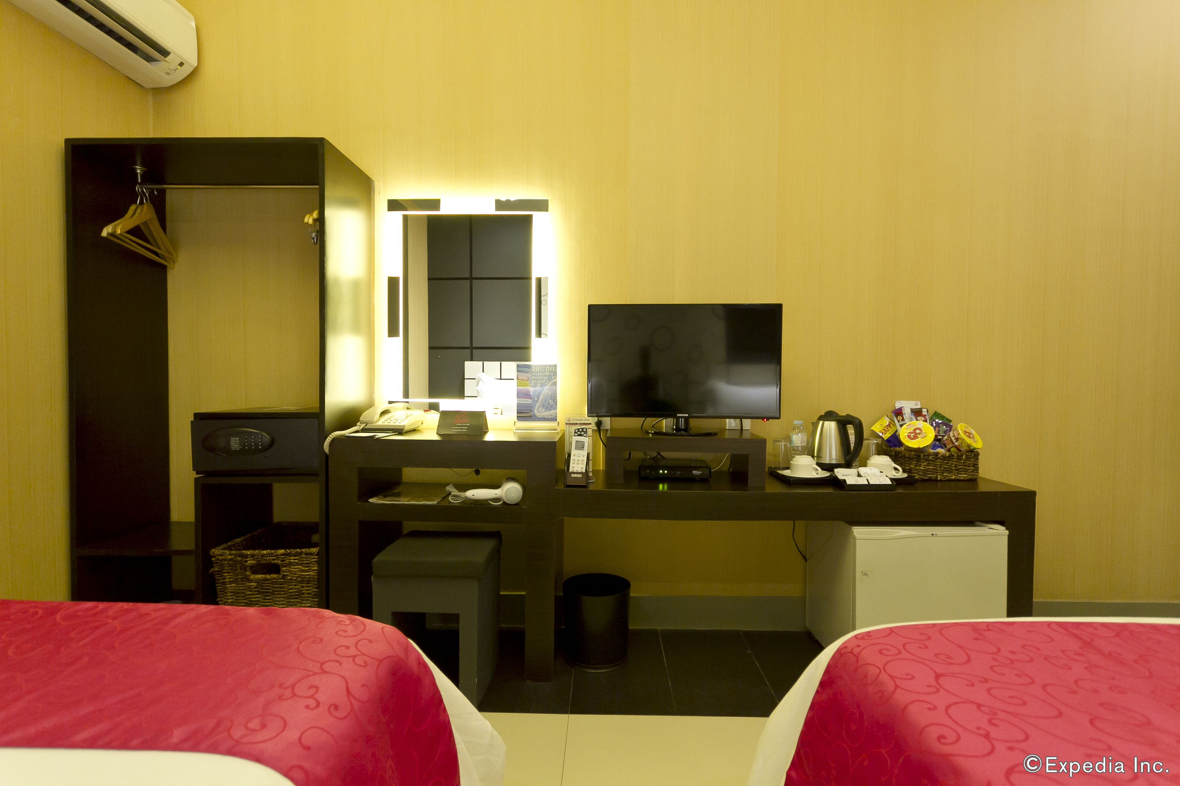 Une chambre d’hôtel avec deux lits, un bureau avec une télévision, un mini-réfrigérateur, un miroir et une petite kitchenette.