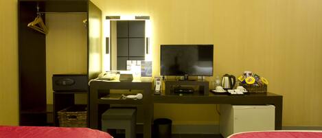 Une chambre d’hôtel avec deux lits, un bureau avec une télévision, un mini-réfrigérateur, un miroir et une petite kitchenette.