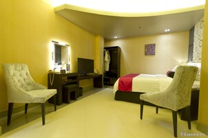 Una habitación de hotel con una cama, dos sillones, un escritorio con televisor y un armario.