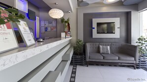 Una moderna zona de recepción con mostrador de mármol, un sofá gris y un televisor montado en la pared.
